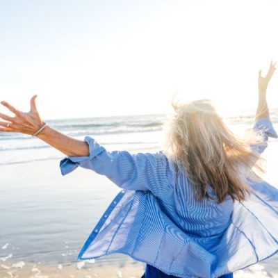 Melanie Liedle-Frau breitet die Arme am Strand aus